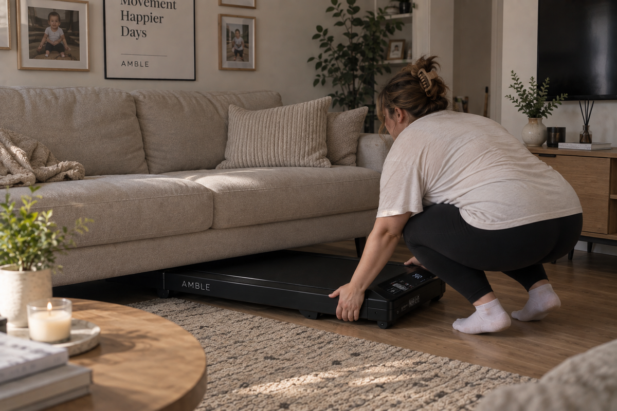 Woman sliding AMBLE Go under a sofa in a living room